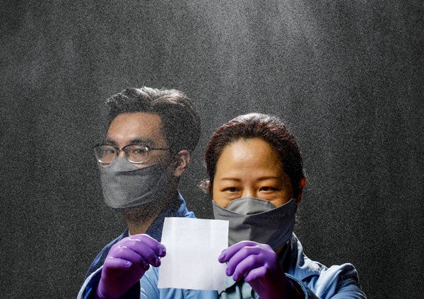 Two researchers, one wearing gloves and holding up a square piece of material