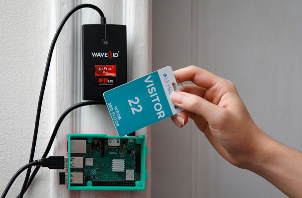 A hand swiping a card through a door-mounted tracker