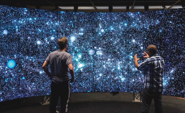 a student and a professor examine a starry-sky-like data visualization in a floor-to-ceiling projection in UIC's Electronic Visualization Lab