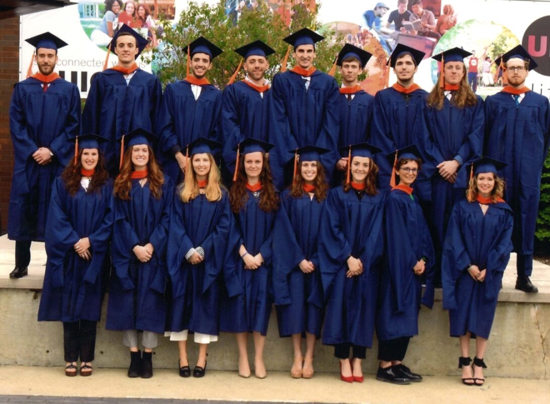 A group of masters students pose for a photo in their graduation gowns on UIC's campus.