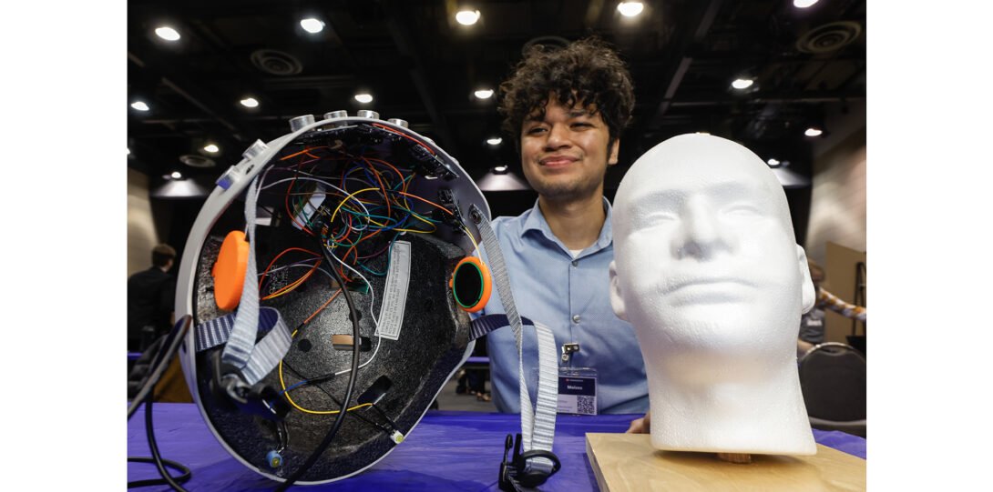 student poses with bicycle helmet outfitted with electronic device