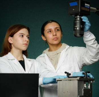 BME students Angela Mitevska (left) and Citlally Santacruz capture high-speed video of stretching a flexible bottomed 96-well plate for strain quantification in a lab.
                  