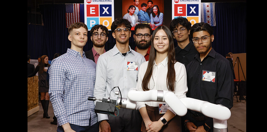 group of students pose standing around robotic arm