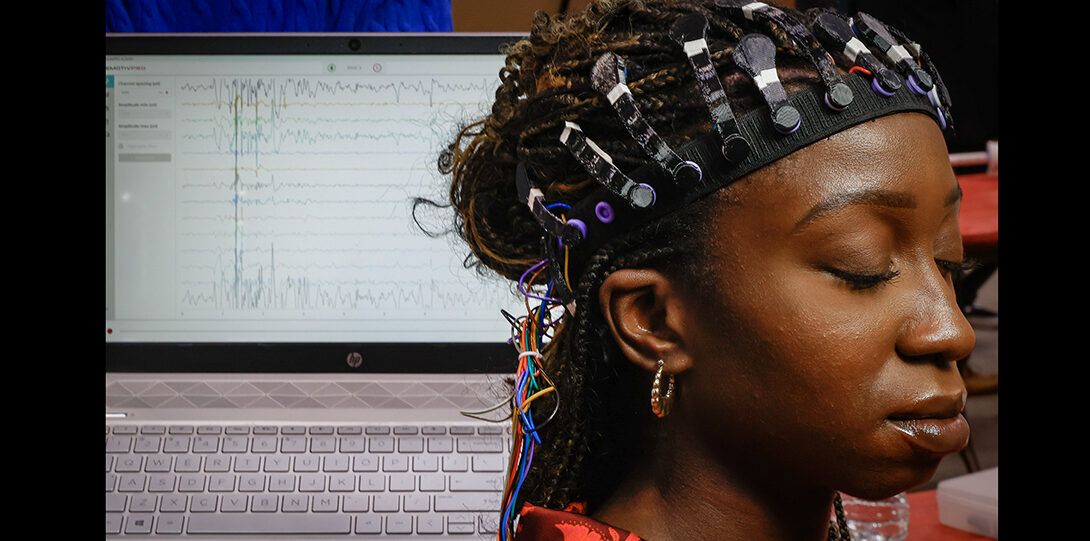 student wears devive on their head with a computer displaying brain wave activity