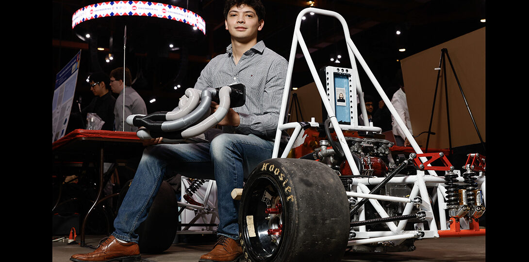 student sitting on a go-cart holding exhaust pipes