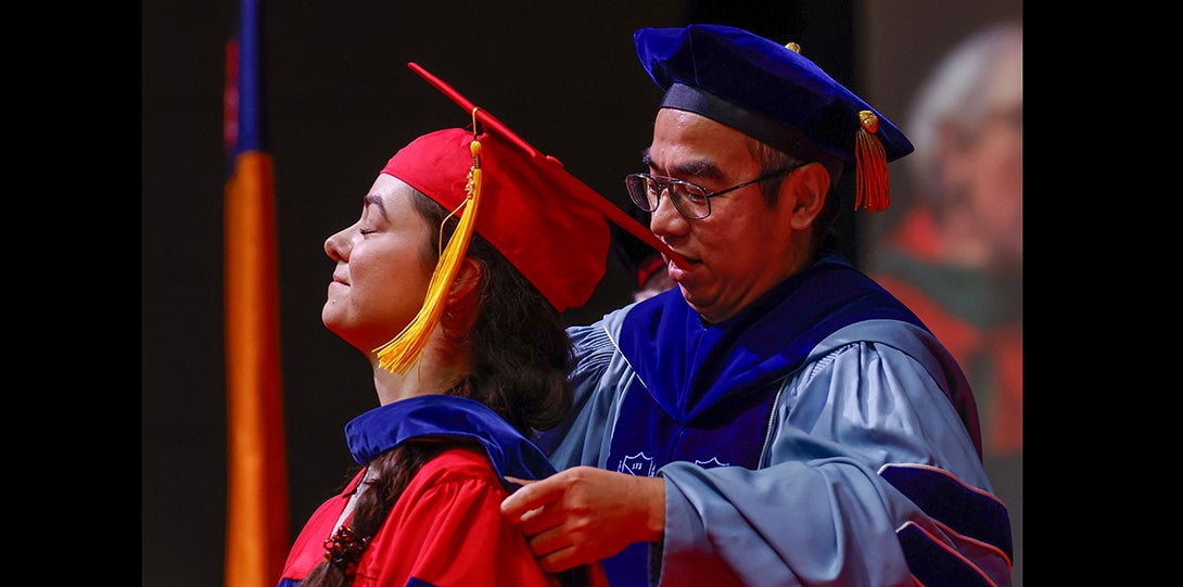 student receives ceremonial hooding from professor