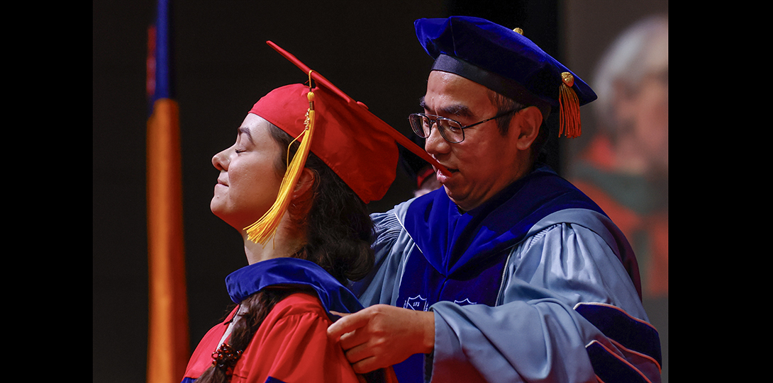 student receives ceremonial hooding from professor