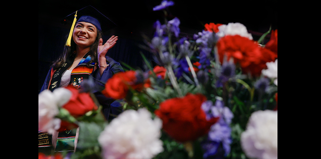 graduating student waves next to flowers