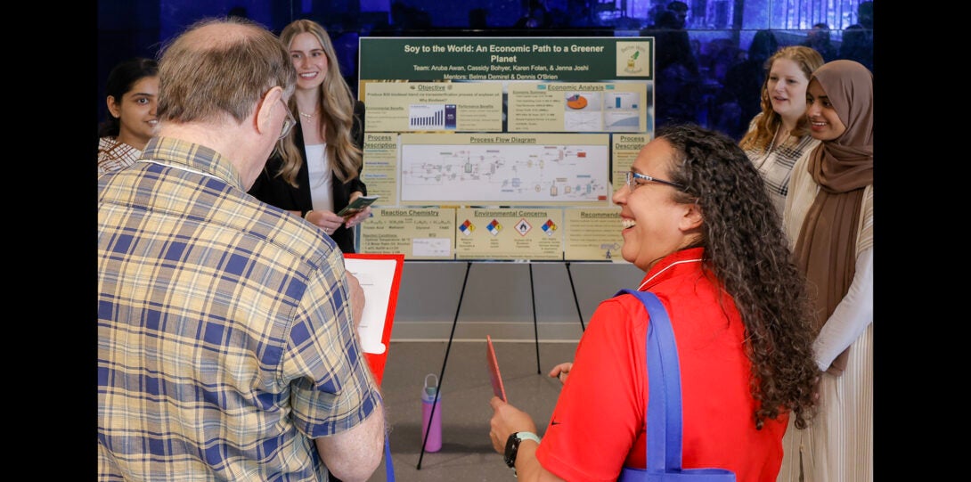 a group of students laugh with judges as they discuss their project poster